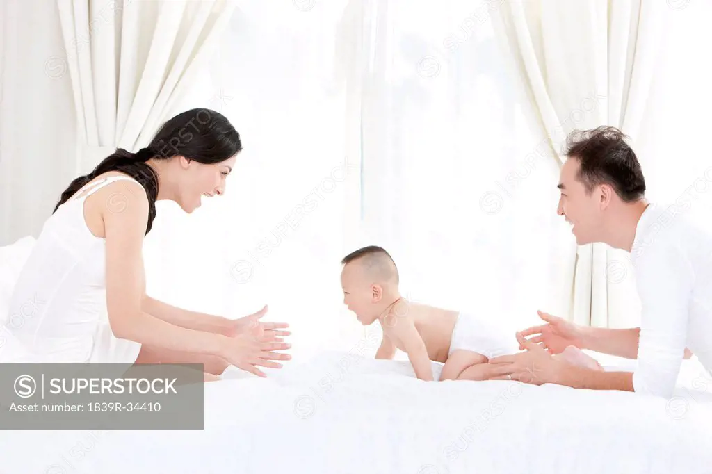 Happy young parents with cute baby in bedroom
