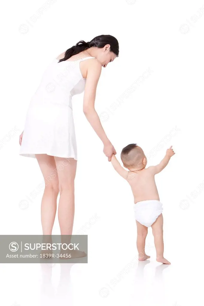 Rear view of young mother teaching baby walking