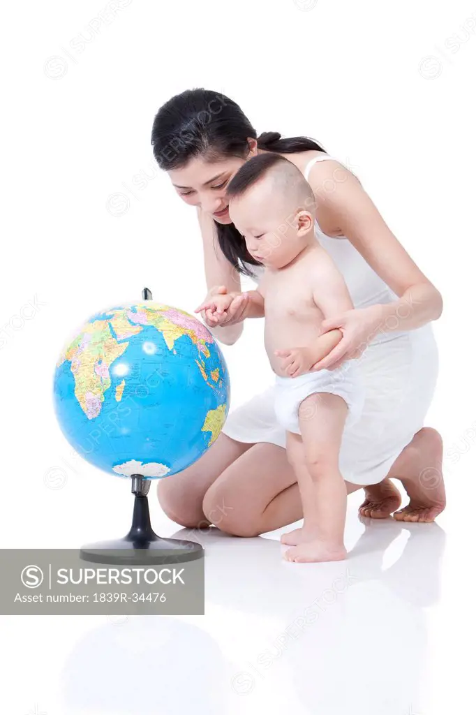 Young mother helping baby learn the places on globe