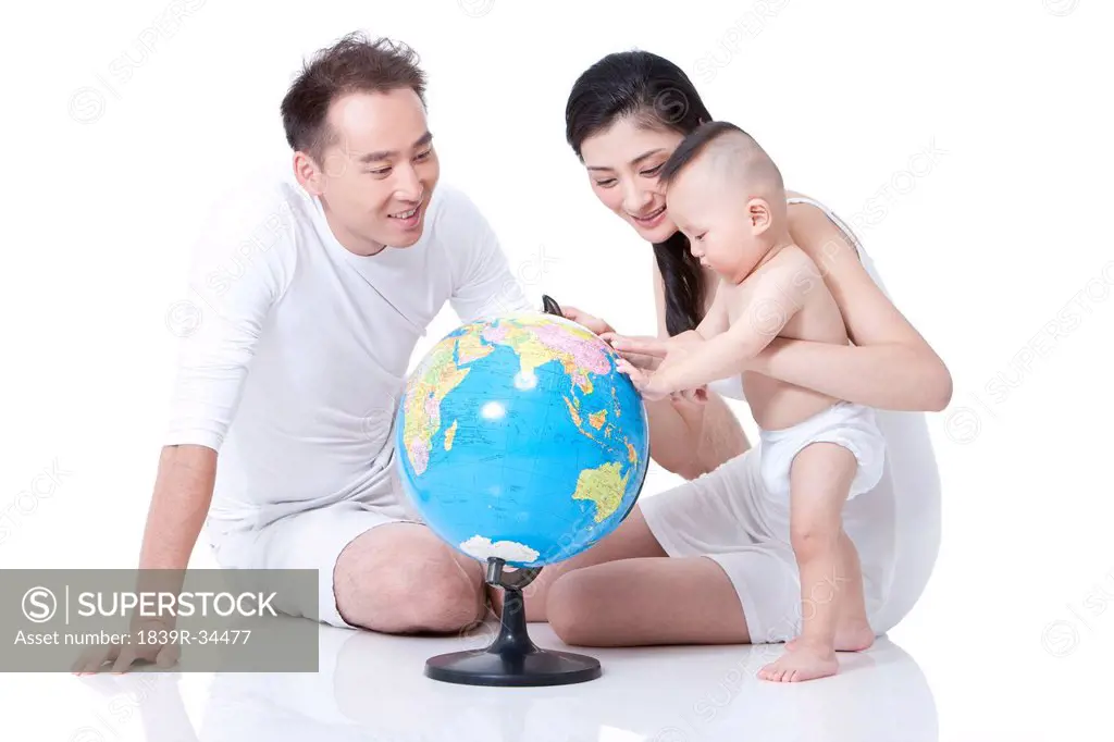 Young parents helping baby learn the places on globe
