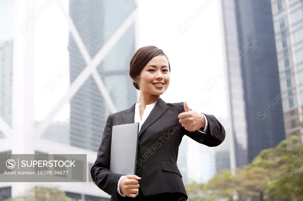 Happy businesswoman doing thumbs up with portfolio in hand, Hong Kong