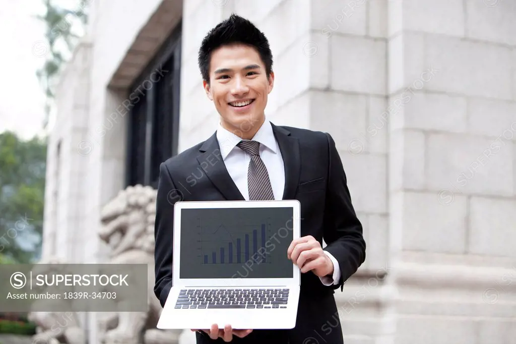 Happy young businessman with a laptop outside a building, Hong Kong