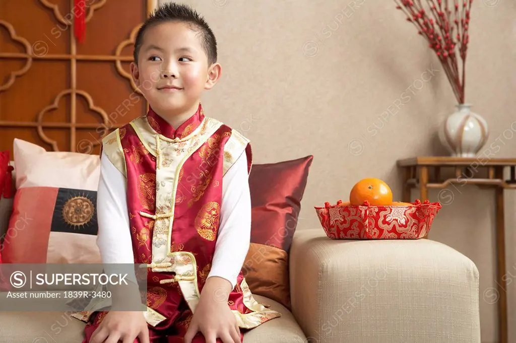 Young Boy Sitting On Couch In Traditional Clothing Looking Mischievous