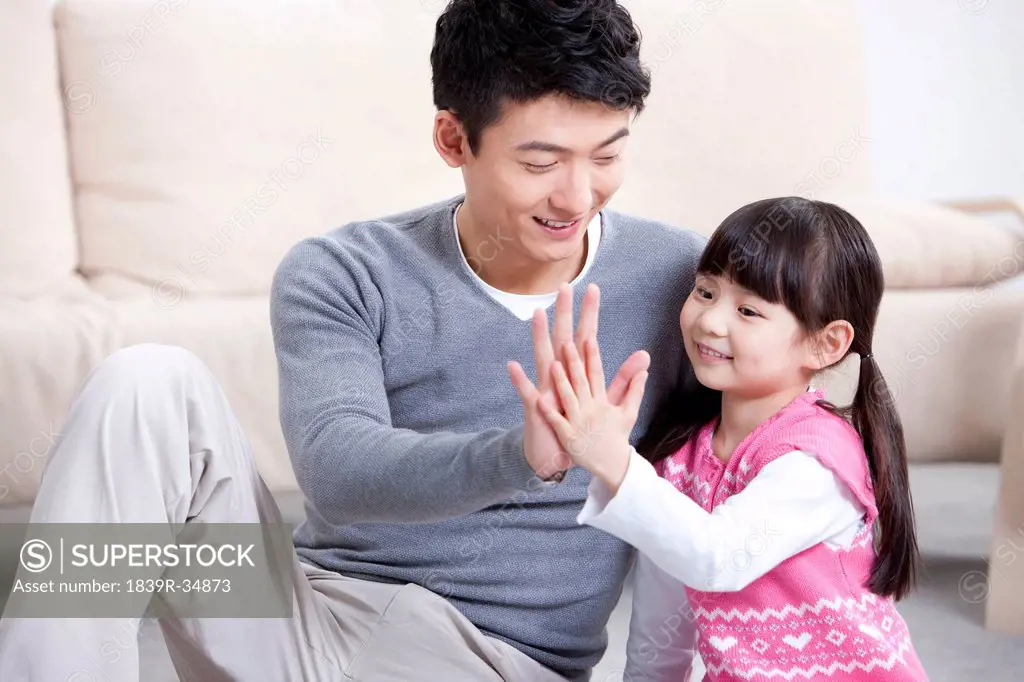 Happy father and little daughter doing high-five at home