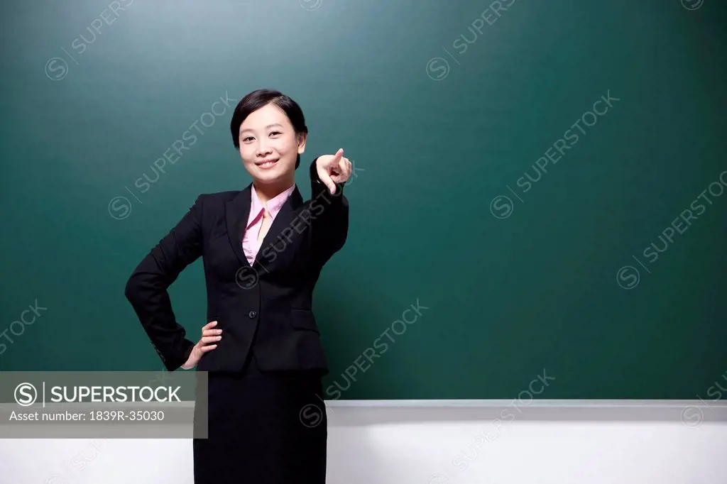 Cheerful female teacher pointing forward in classroom
