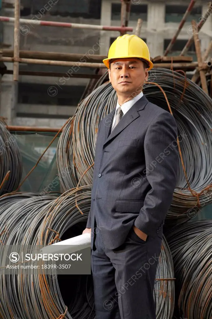 Businessman In A Construction Site Wearing A Hard Hat And Holding Plans