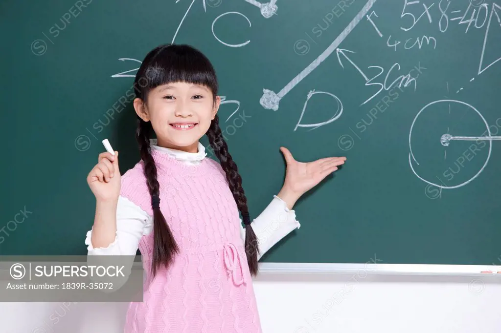Cute little girl writing on blackboard