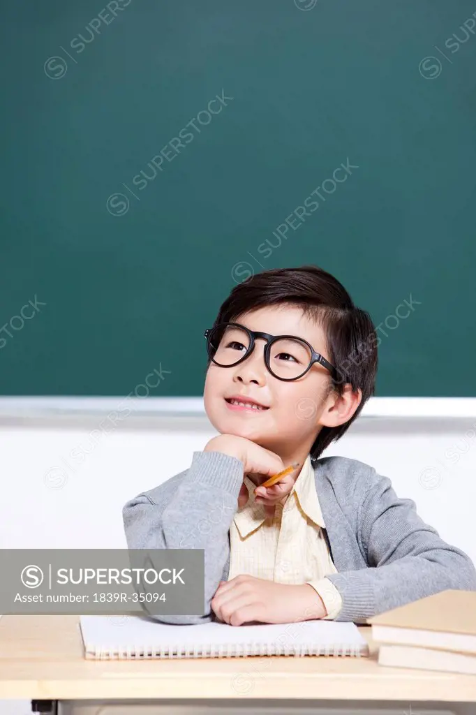 Cute schoolboy thinking hand on chin in classroom