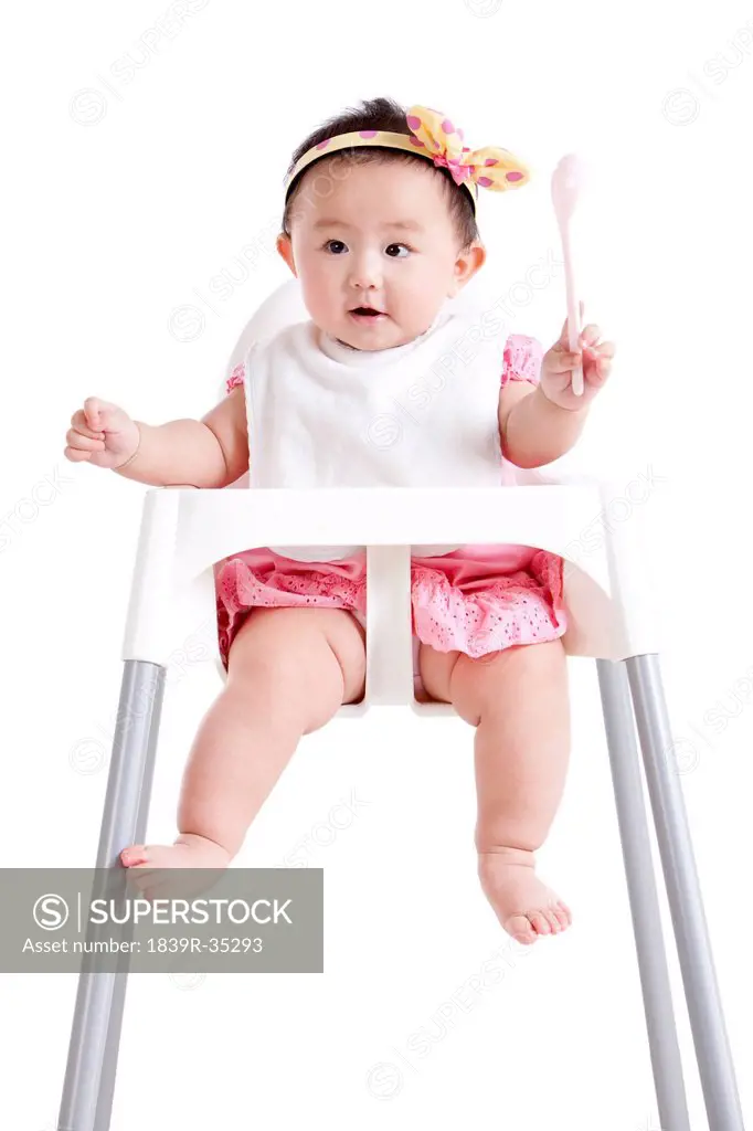 Adorable baby girl with a spoon on baby high chair