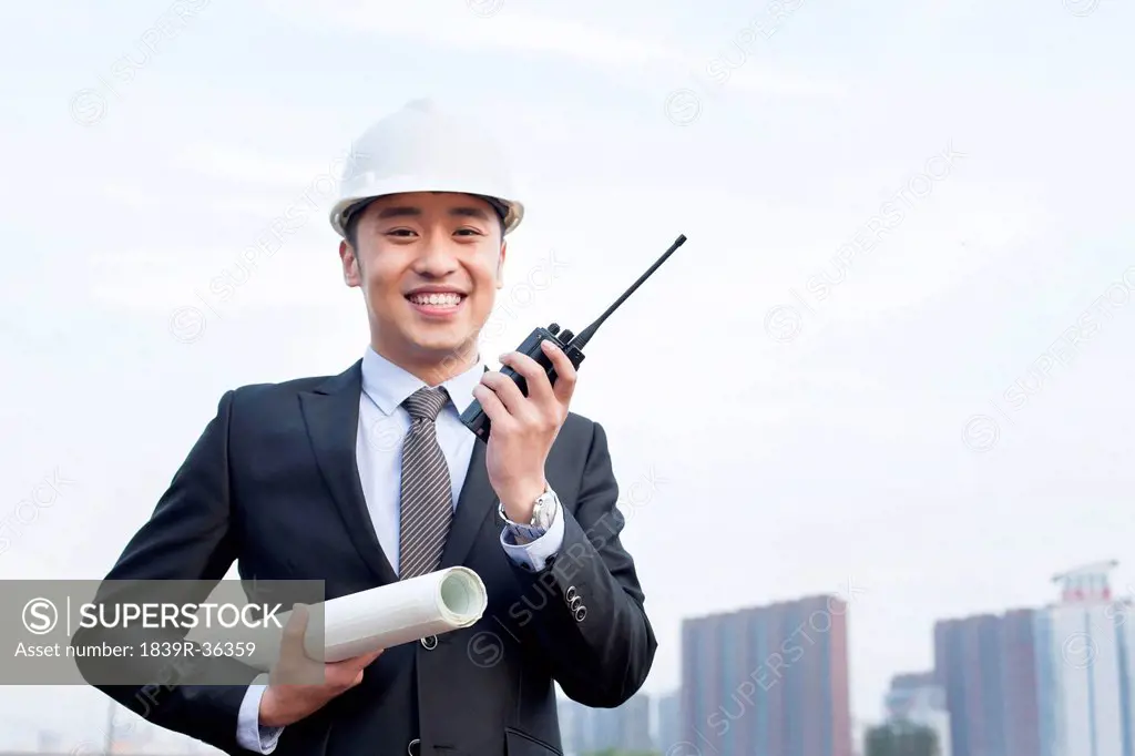 Young male architect with intercom and blueprint outdoors