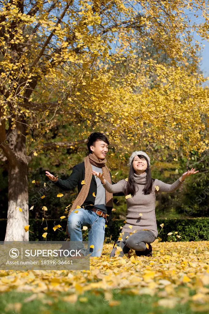 Happy young couple enjoying the dancing fallen leaves in the fall