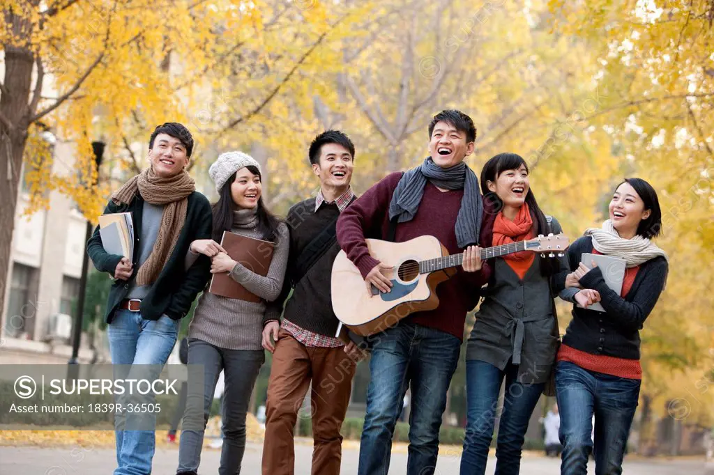 College students walking and playing guitar on campus in autumn