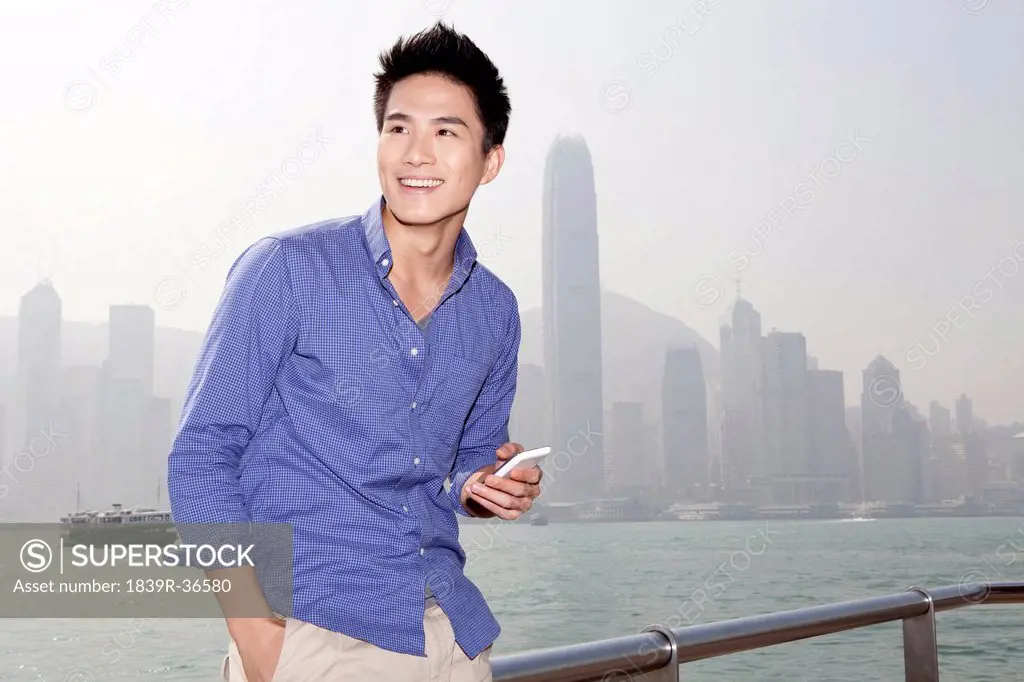Happy young man with smart phone in Victoria Harbor, Hong Kong