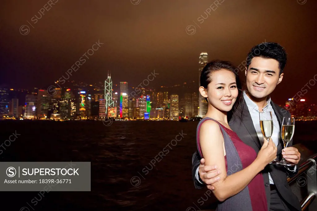 Happy young couple enjoying the night view of Victoria Harbor with champagne, Hong Kong
