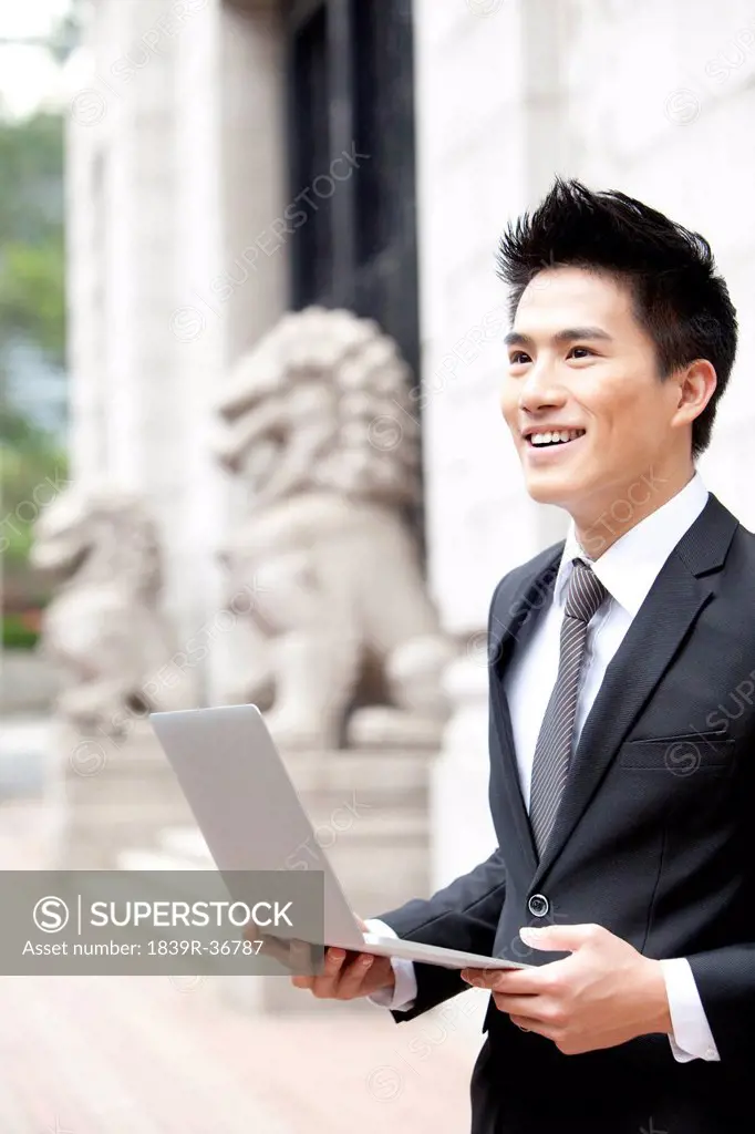 Cheerful young businessman with a laptop outside a building, Hong Kong