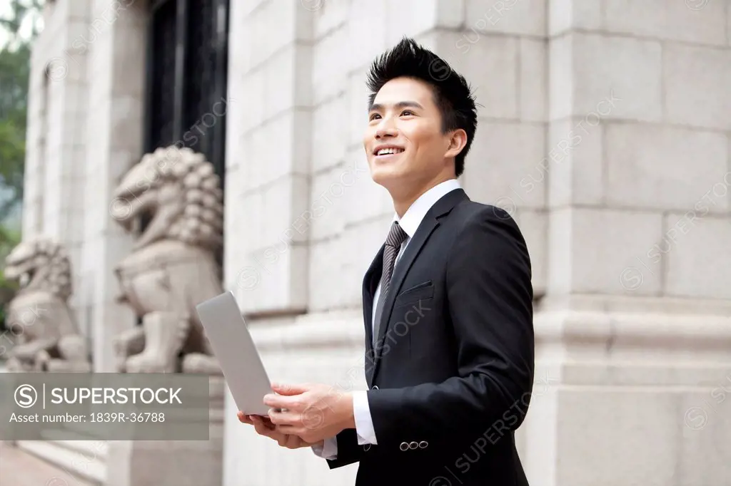 Cheerful young businessman with a laptop outside a building, Hong Kong