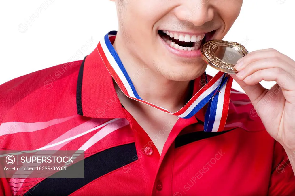 Male athlete biting gold medal celebrating victory
