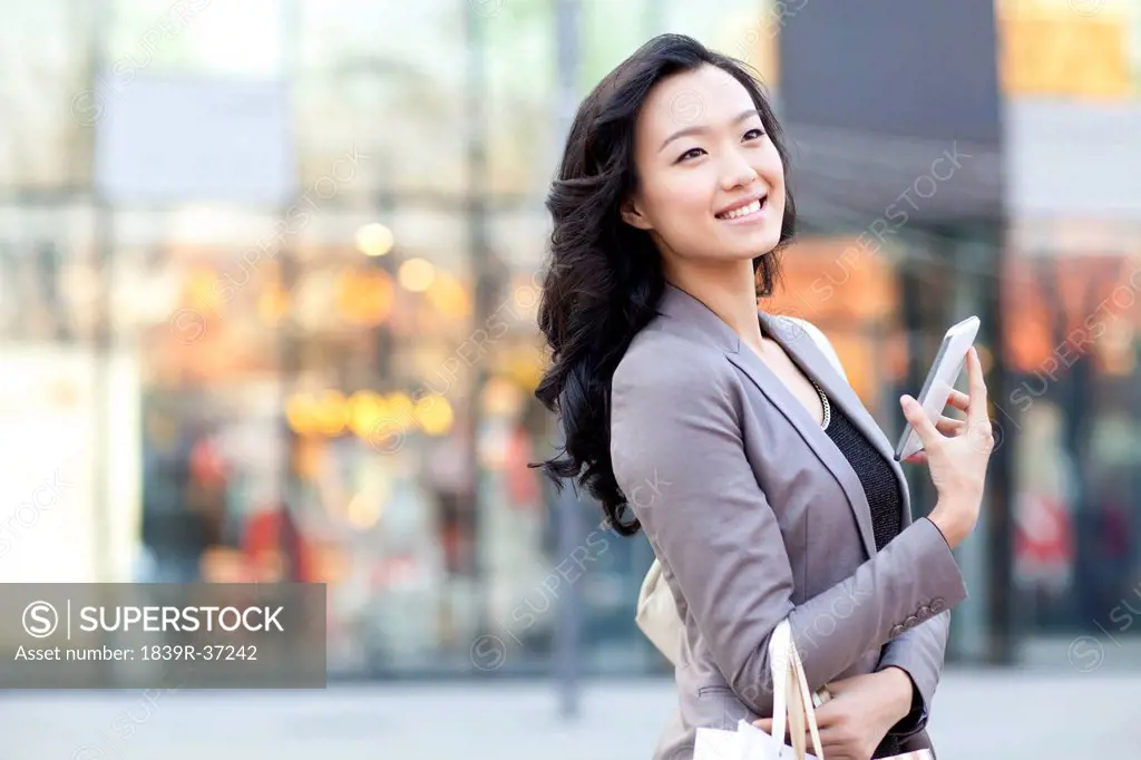 Happy young woman with smart phone in city street