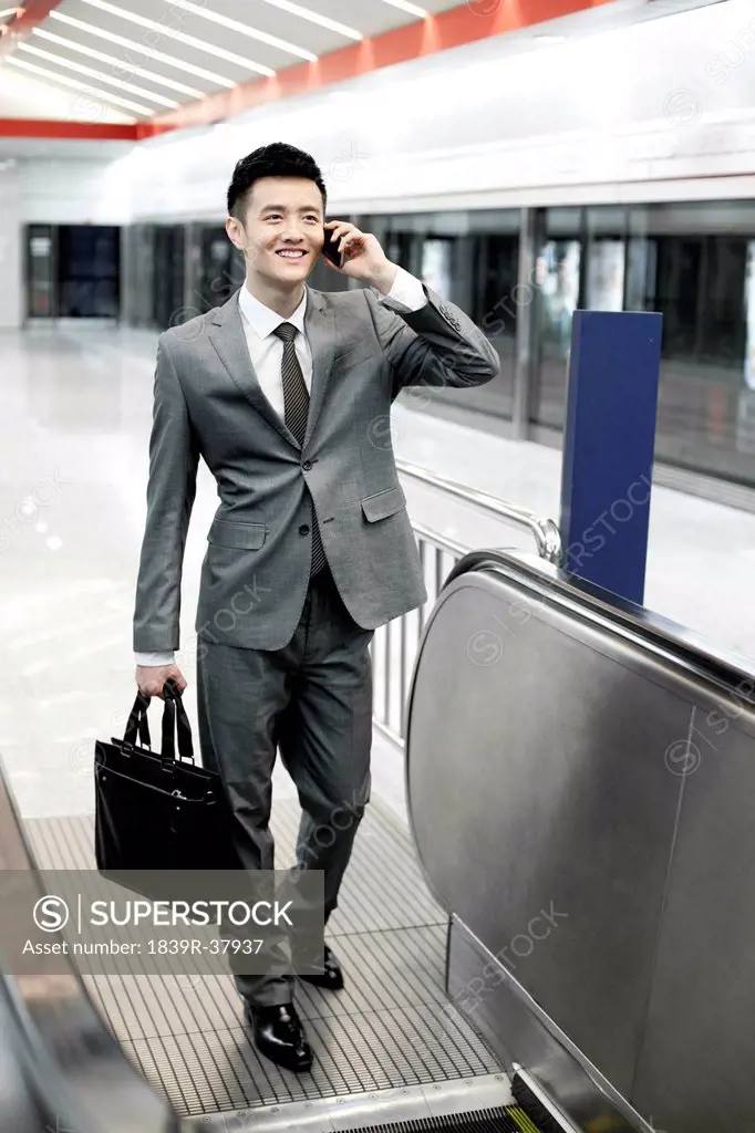 Businessman on the phone and taking escalator at subway station