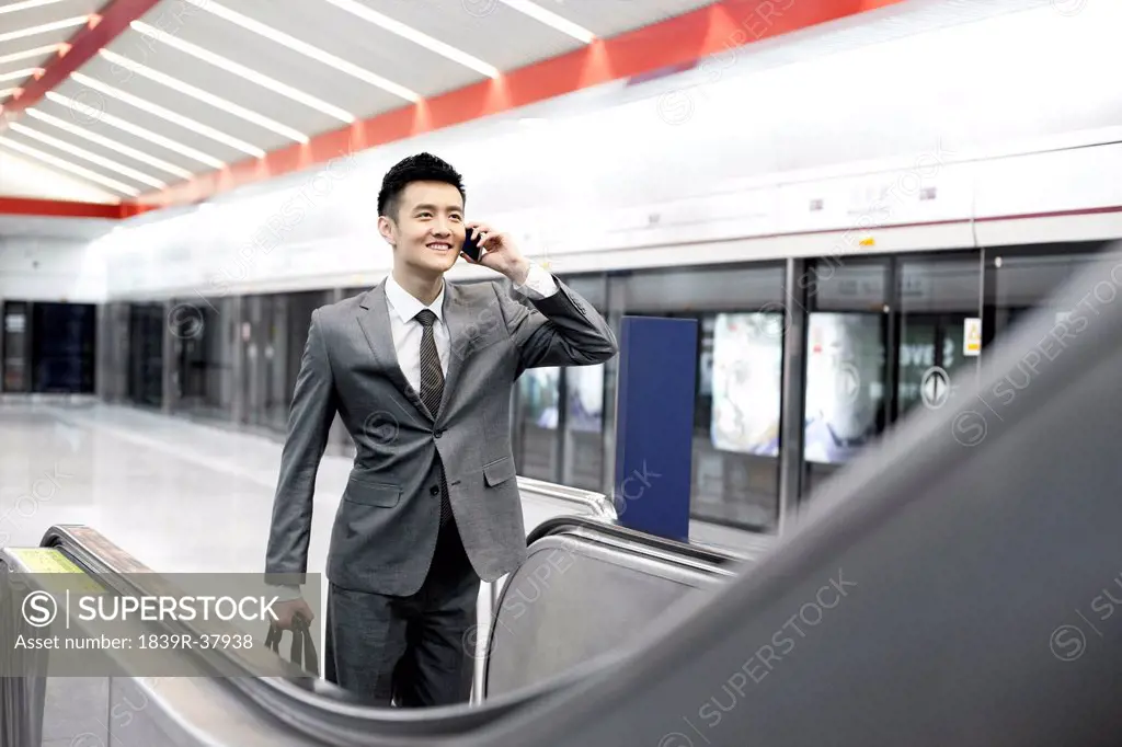 Businessman on the phone and taking escalator at subway station