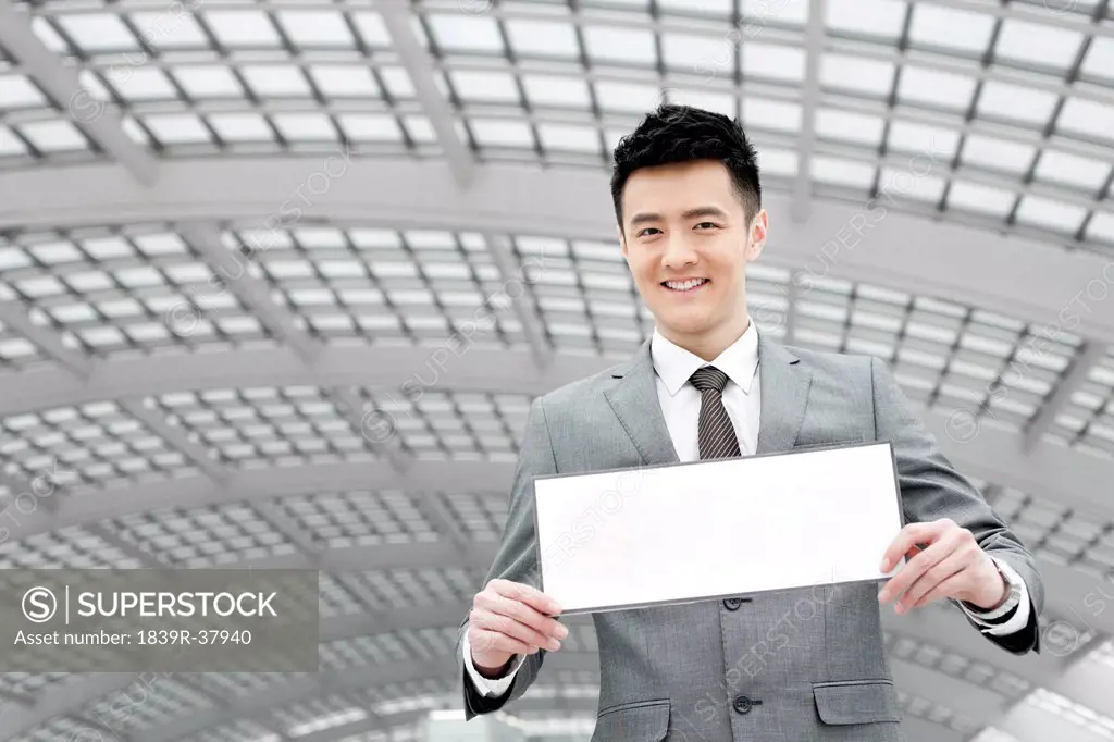 Chinese businessman holding blank sign in airport lobby