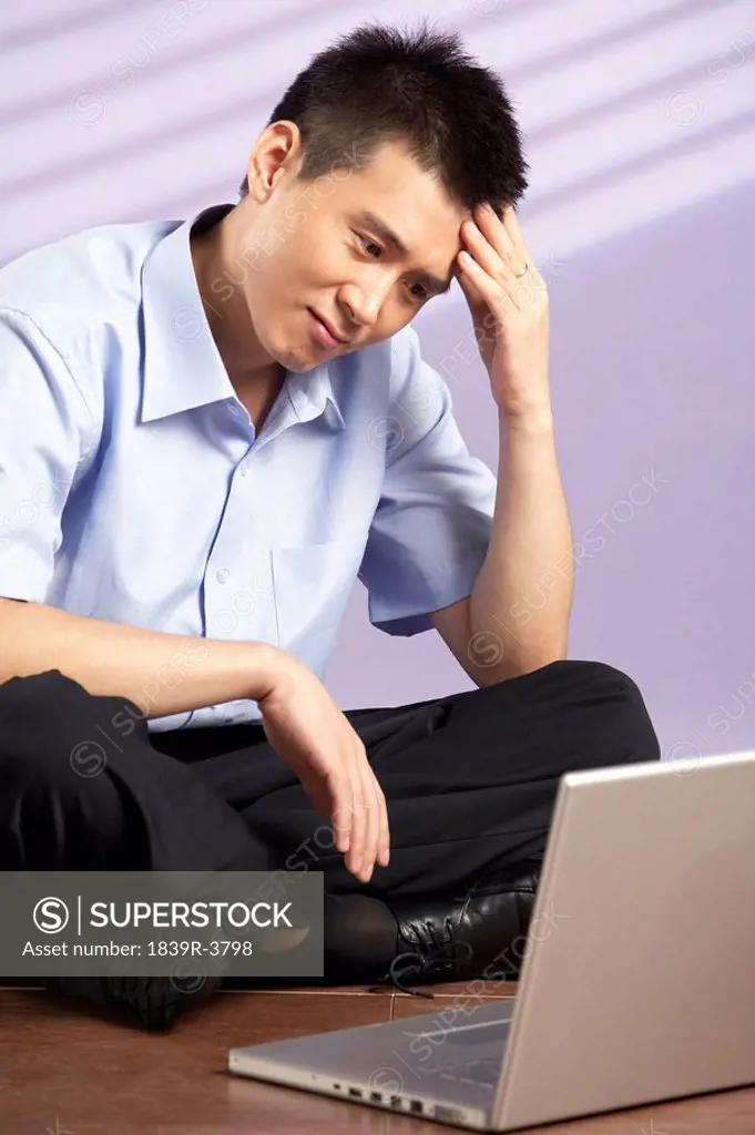Man Sitting On Floor With A Computer Looking Frustrated
