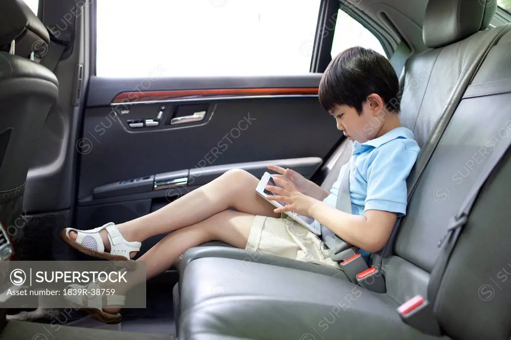Cute boy playing digital tablet in car back seat