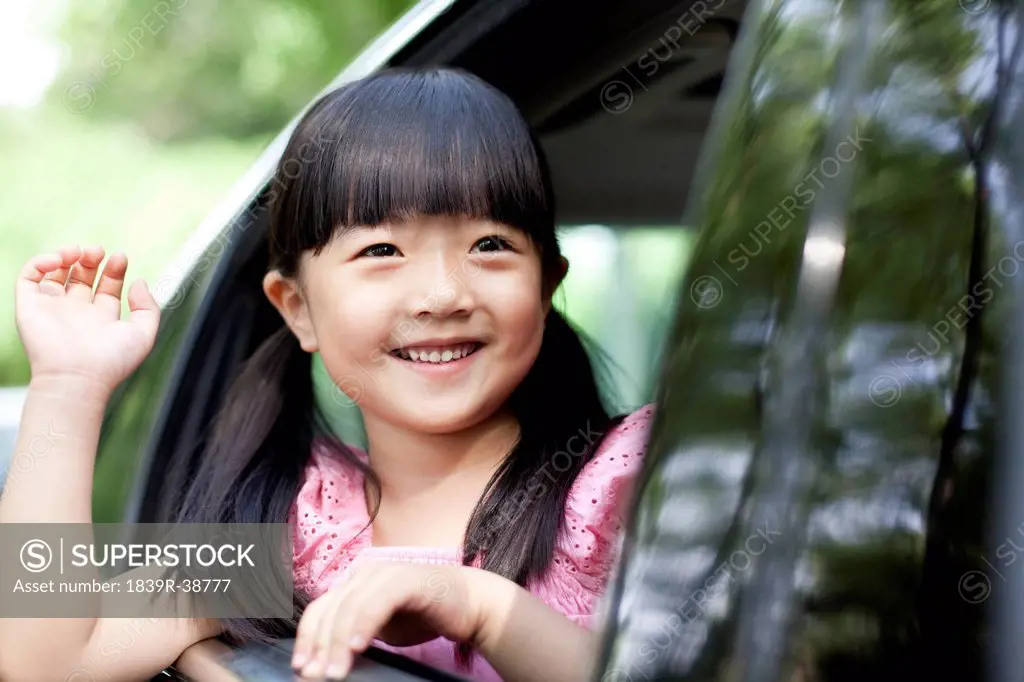 Cheerful girl waving out of car window