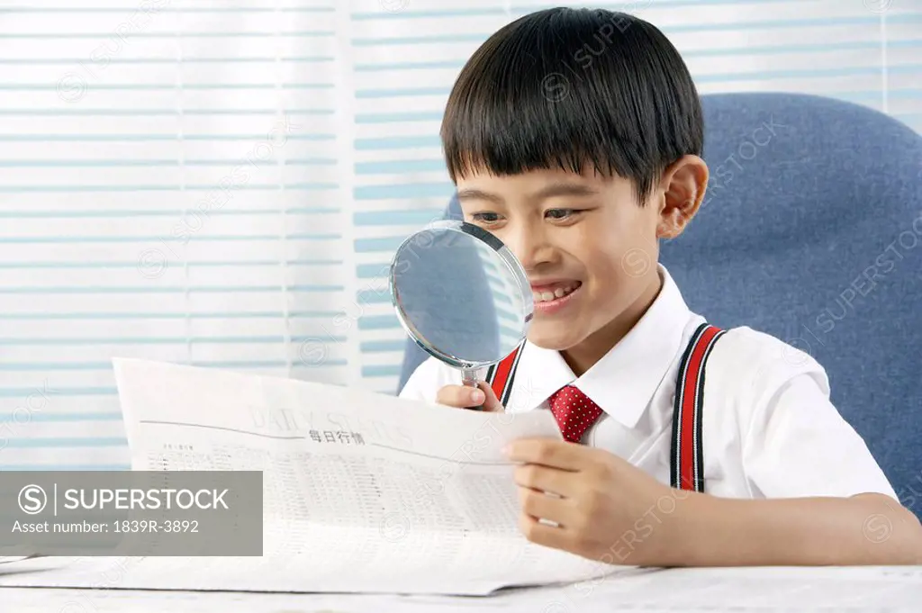Young Boy Reading Paper With A Magnifying Glass
