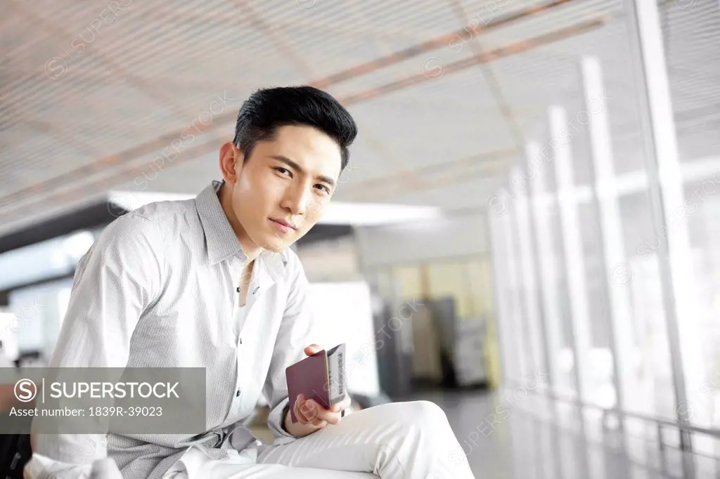 Young man waiting in airport lounge with flight ticket and passport