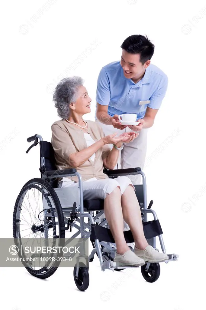 Male nursing assistant handing wheelchair bound woman a cup of coffee