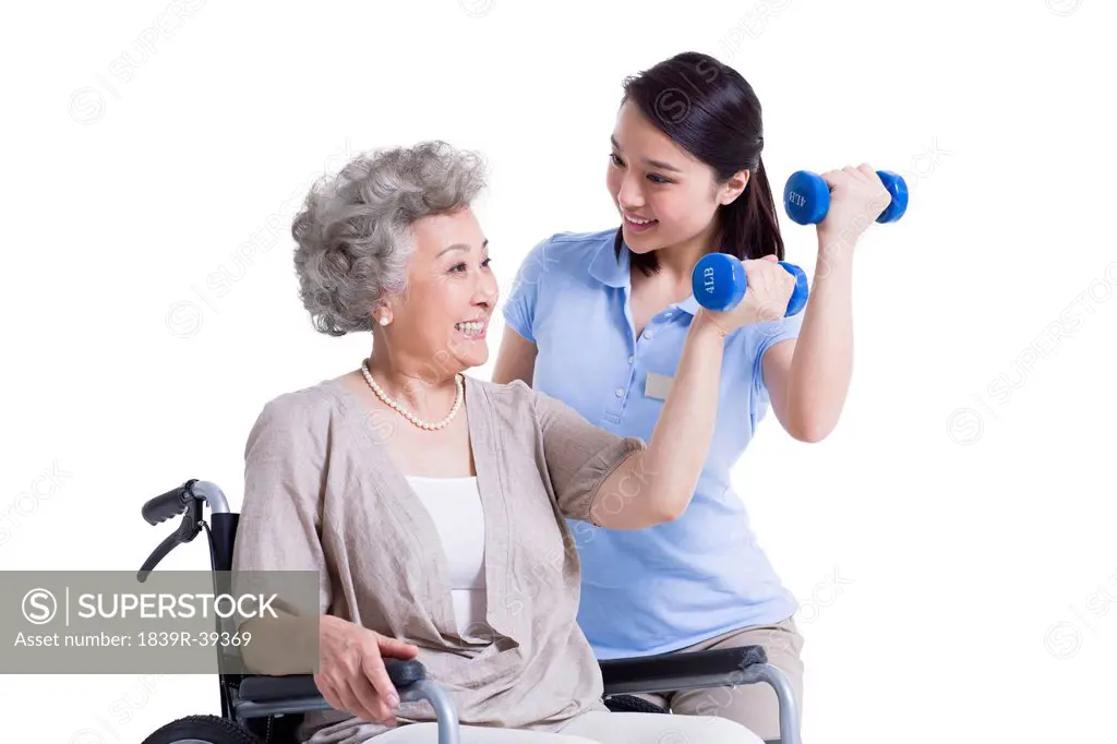Female nursing worker helping senior woman doing exercise