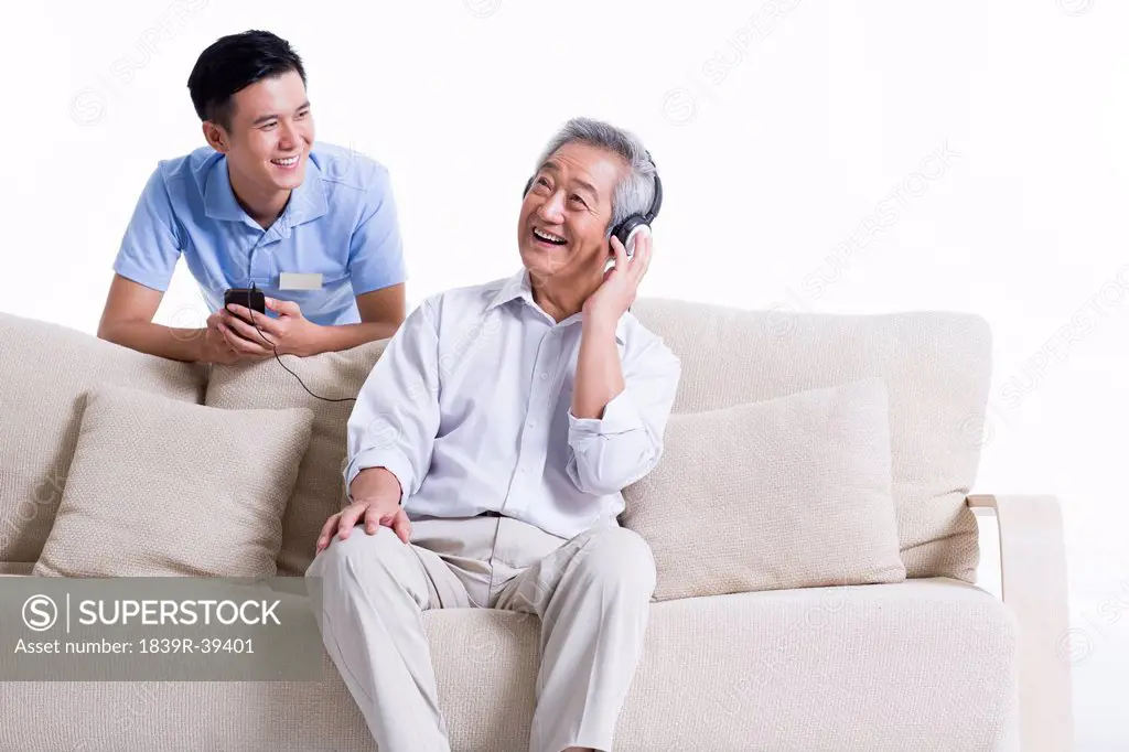 Senior man listening to music with nursing assistant's company