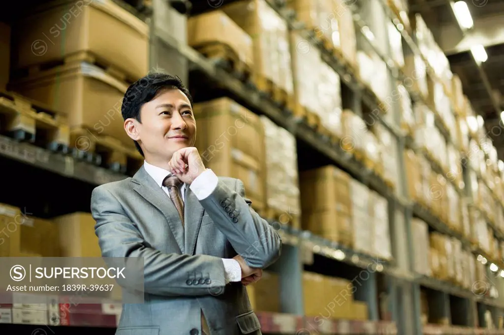 Confident businessman hand on chin in warehouse