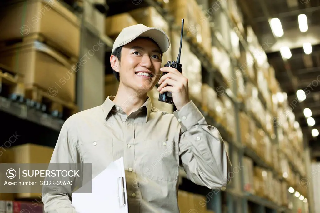 Young logistics staff using walkie-talkie in warehouse