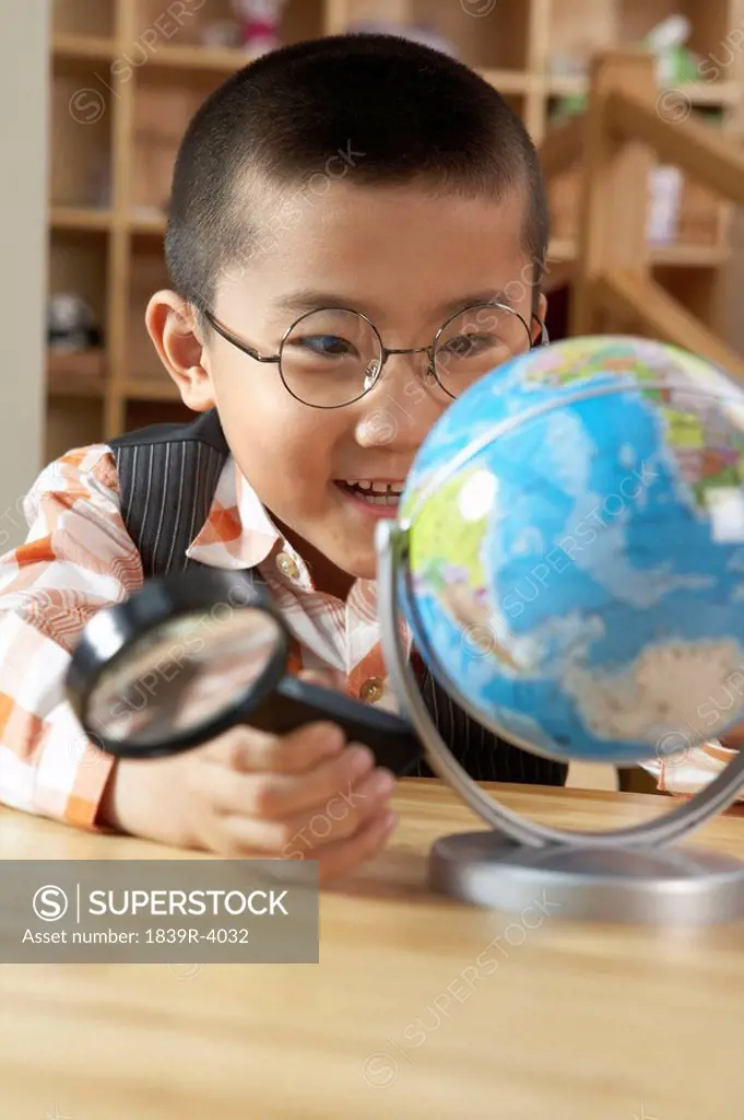 Young Boy Studying A Globe With A Magnifying Glass