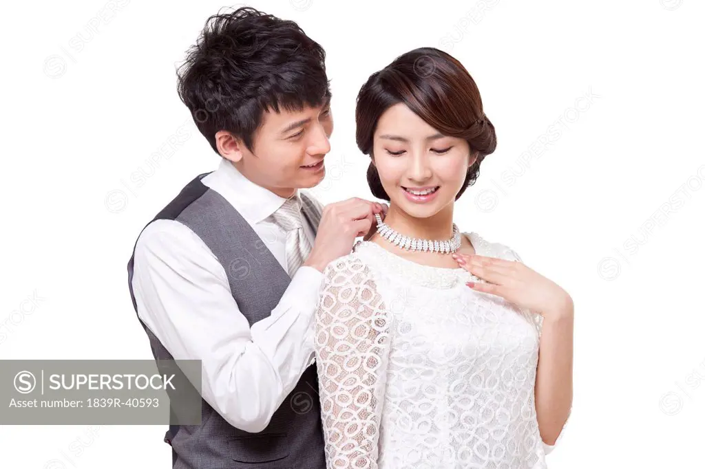 Happy young man fastening young woman's diamond necklace
