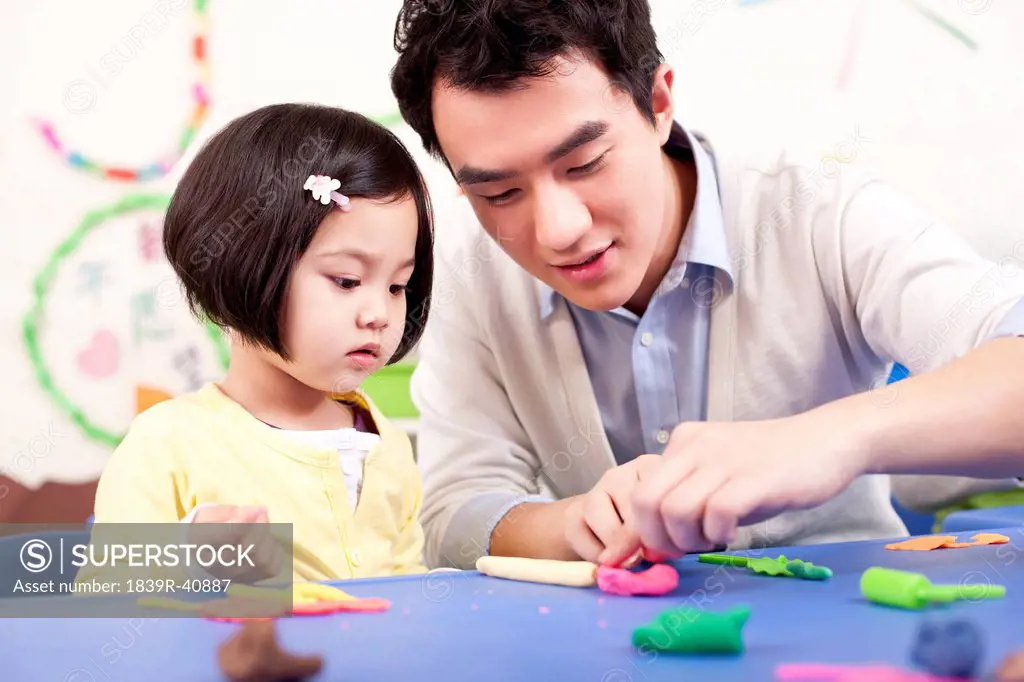 Kindergarten teacher and lovely girl playing with child's play clay