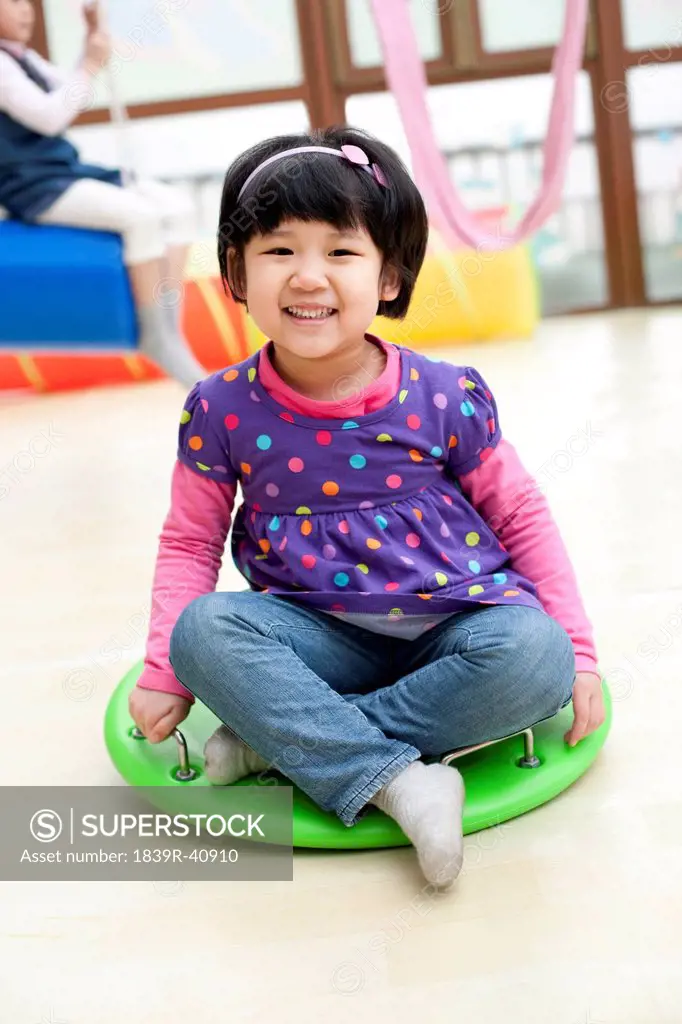 Cute girl sitting on a big toy dreidel in kindergarten