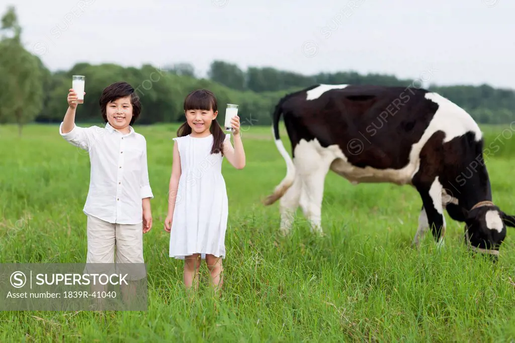 Happy children holding glasses of milk with cattle grazing in the pasture