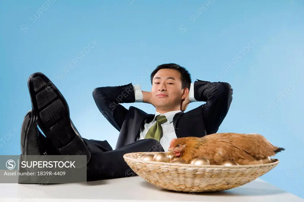 Businessman Relaxing Next To Chicken And Golden Eggs