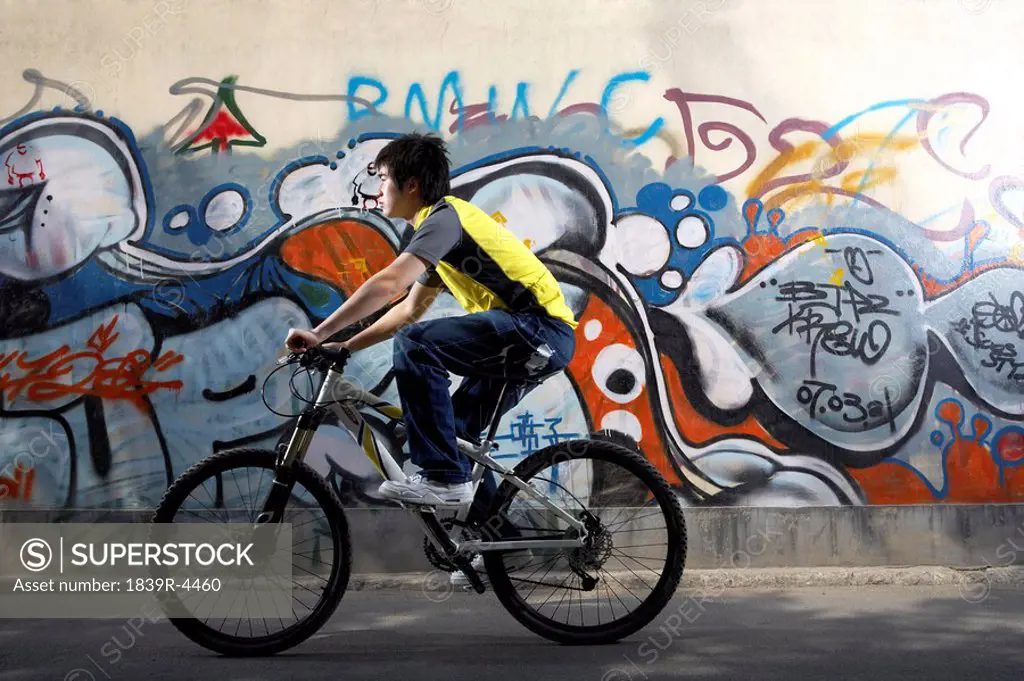 Teenage Boy Riding A Bike Past Graffiti
