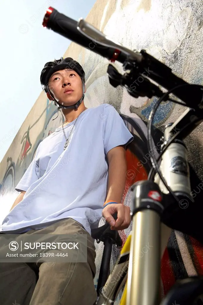 Teenage Boy Leaning On Bike In Front Of A Wall Of Graffiti