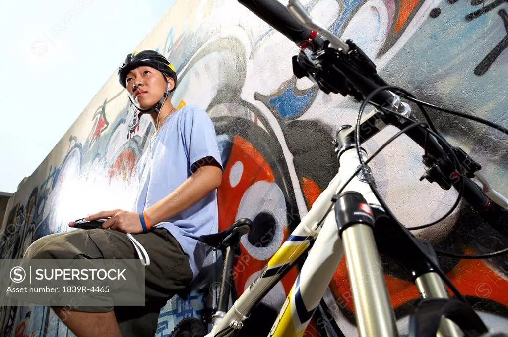 Teenage Boy Leaning On Bike Holding Game Console