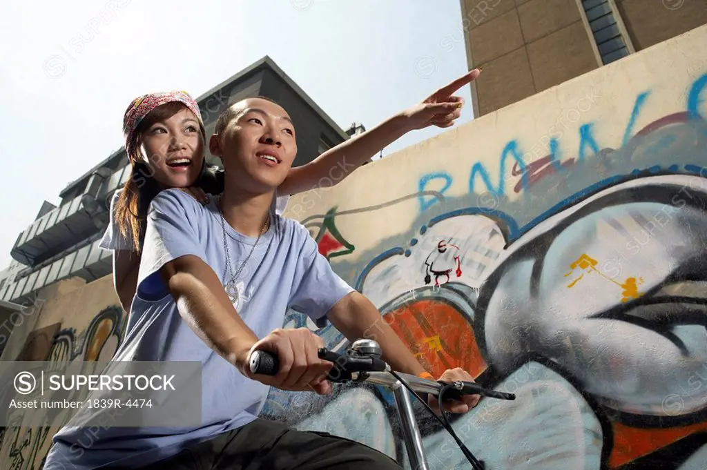 Teenage Boy And Girl On Bike In Front Of A Wall Of Graffiti