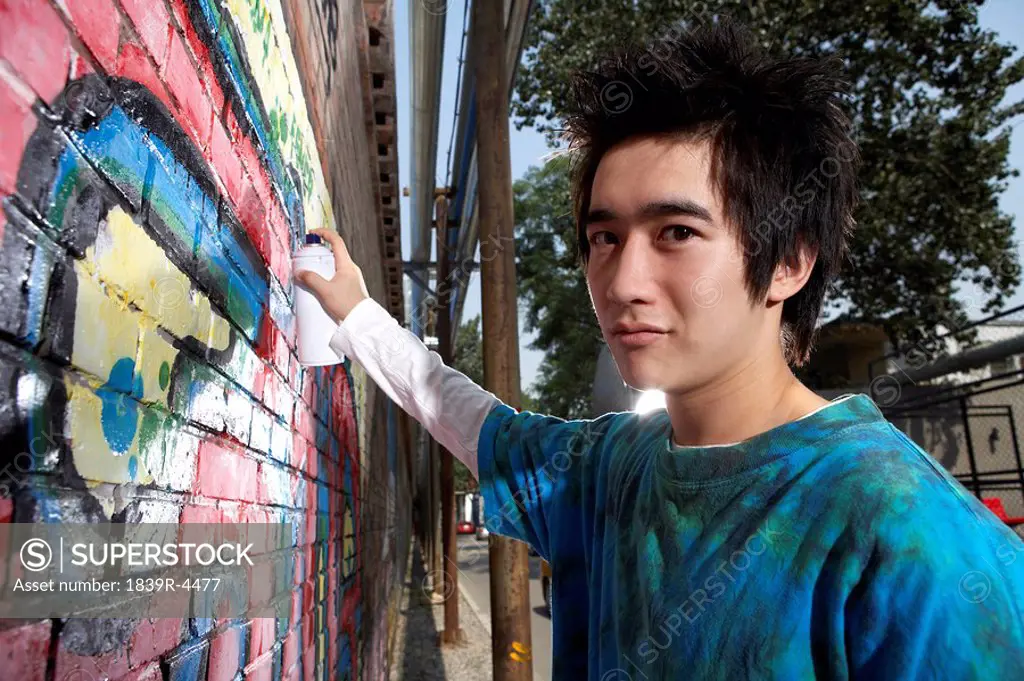 Teenage Boy Spraying Graffiti On A Wall