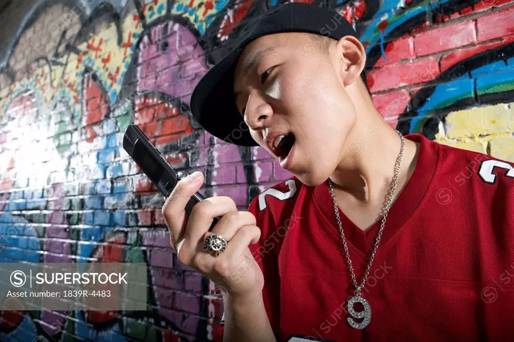Teenage Boy Yelling Into A Cellphone In Front Of A Wall Of Graffiti
