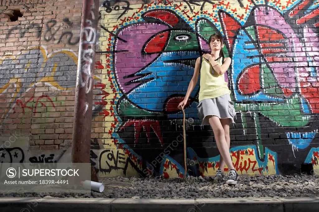 Teenage Girl With Skateboard Leaning On A Wall Of Graffiti
