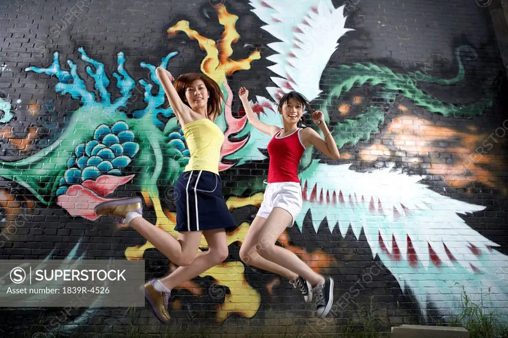 Teenage Girls Jumping Next To Spray Painted Mural