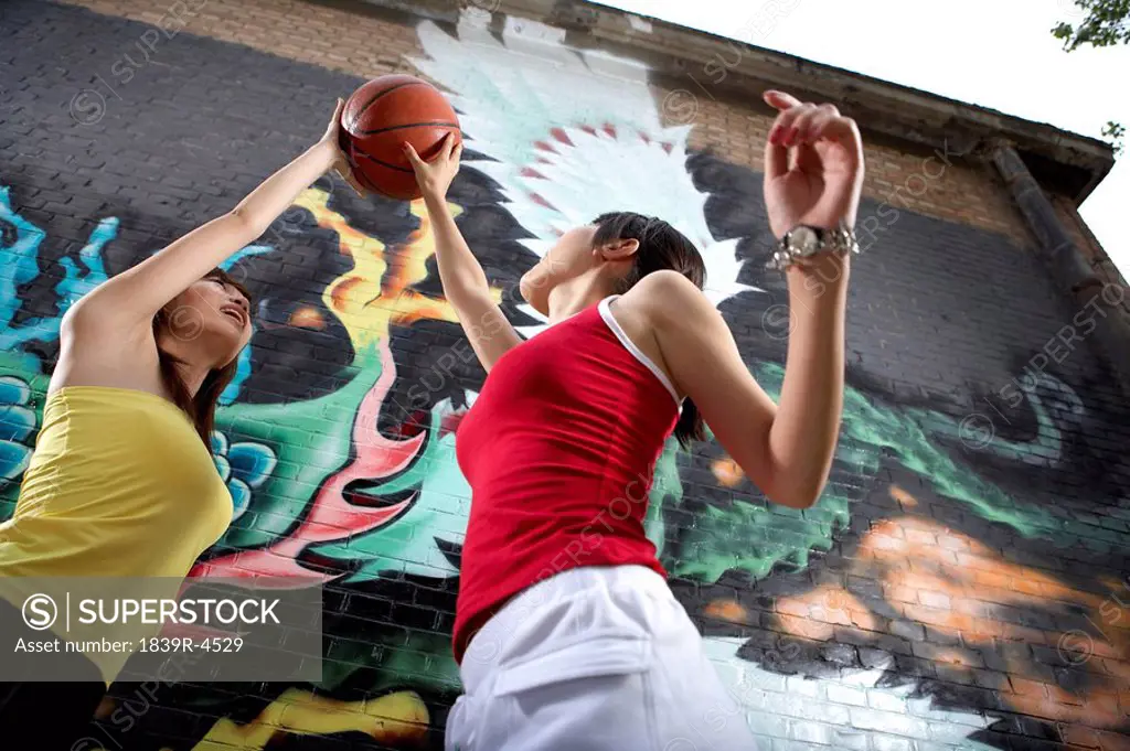 Teenage Girls Playing Basketball Next To Spray Painted Mural